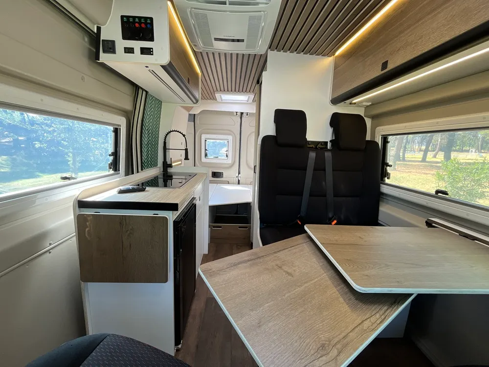 Interior de la camper Jumper L2H2 con mesa, asientos giratorios y cocina lateral