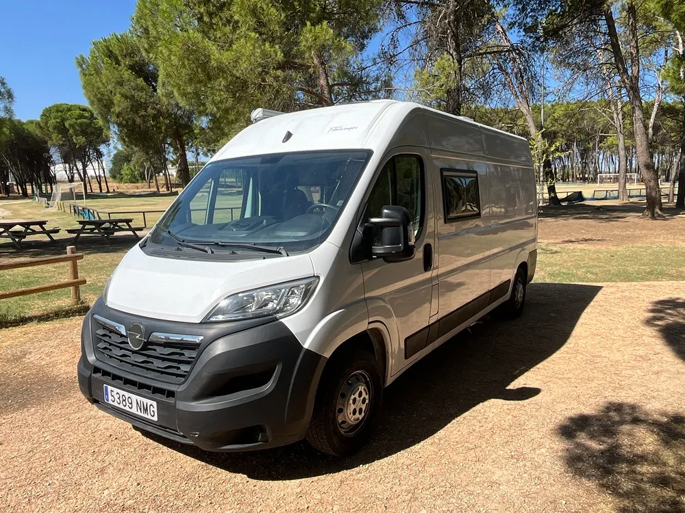 Furgoneta camper Opel Movano L3H2 vista desde el frontal izquierdo en un pinar