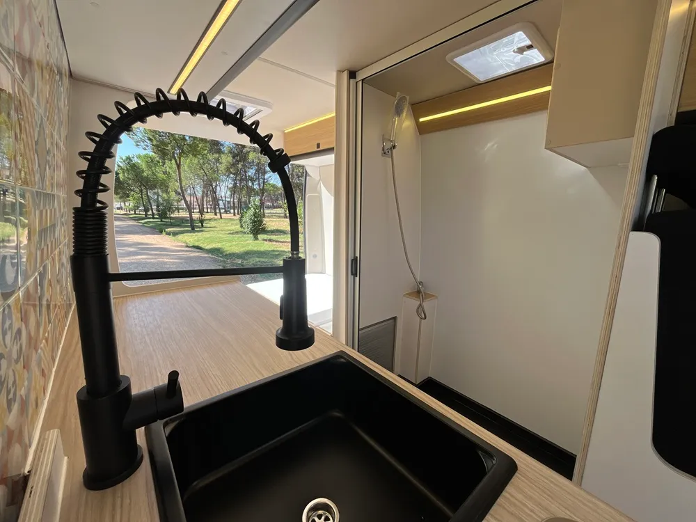 Fregadero negro con grifo extraíble y frente de azulejo hidráulico en la cocina camper