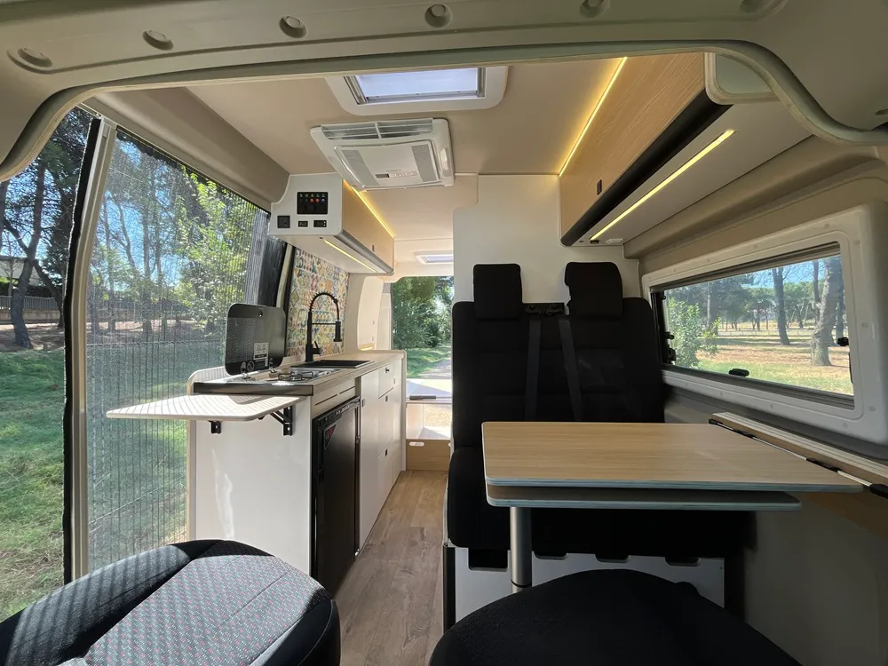 Interior de la camper Movano L3H2 con cocina, mesa abatible y asientos giratorios