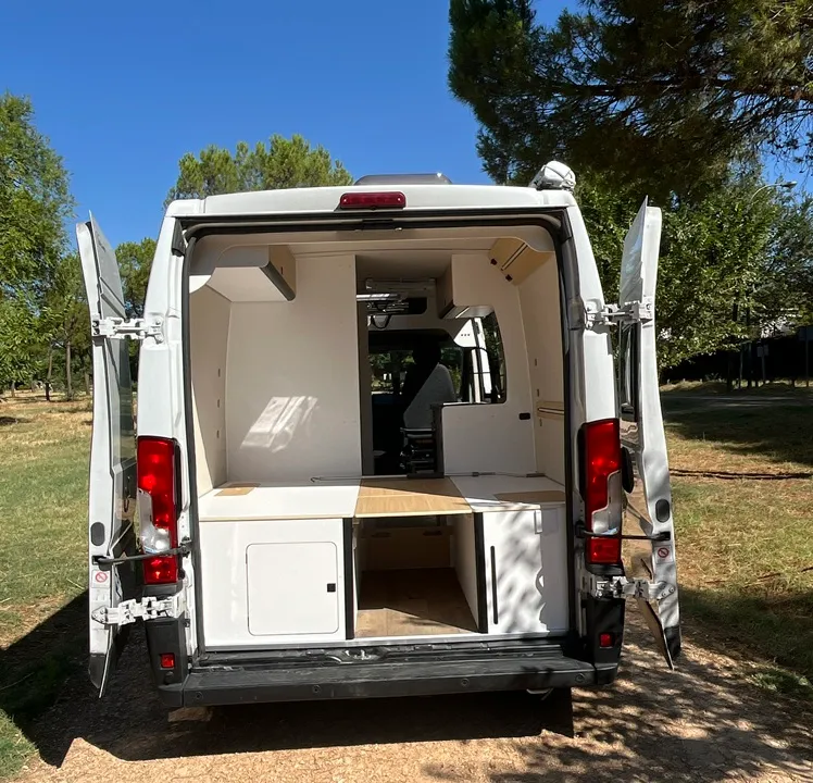 Trasera abierta del Opel Movano camper con maletero bajo la cama y muebles en blanco